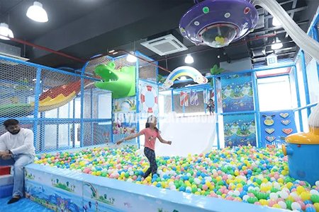 Children playing in a vibrant ball pit area of an indoor playground in India.