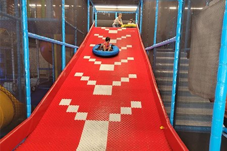 Children sliding down a dry snow slide in an indoor playground.