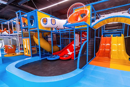 Children playing in a soft play area with colorful foam shapes in an indoor playground.